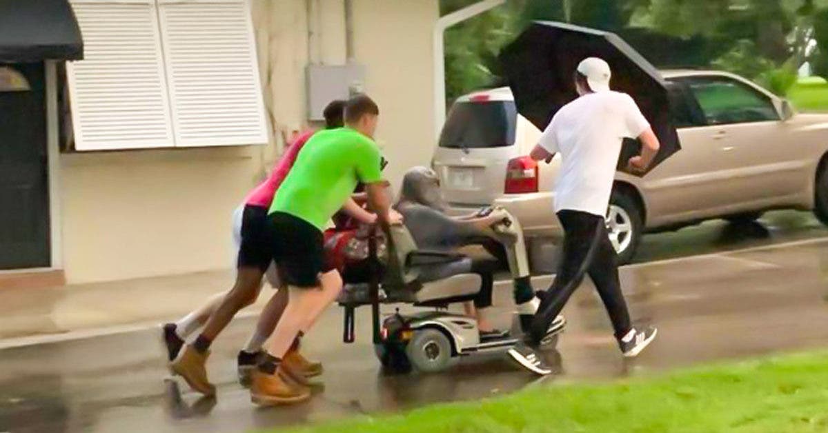 Ces jeunes hommes poussent le fauteuil électrique d'une femme âgée jusqu'à sa maison de retraite après qu'il soit tombé en panne sous la pluie