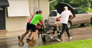 Ces jeunes hommes poussent le fauteuil électrique d'une femme âgée jusqu'à sa maison de retraite après qu'il soit tombé en panne sous la pluie