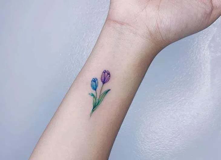 Tatouage de deux petites fleurs colorées en rose et en bleu sur l’avant bras
