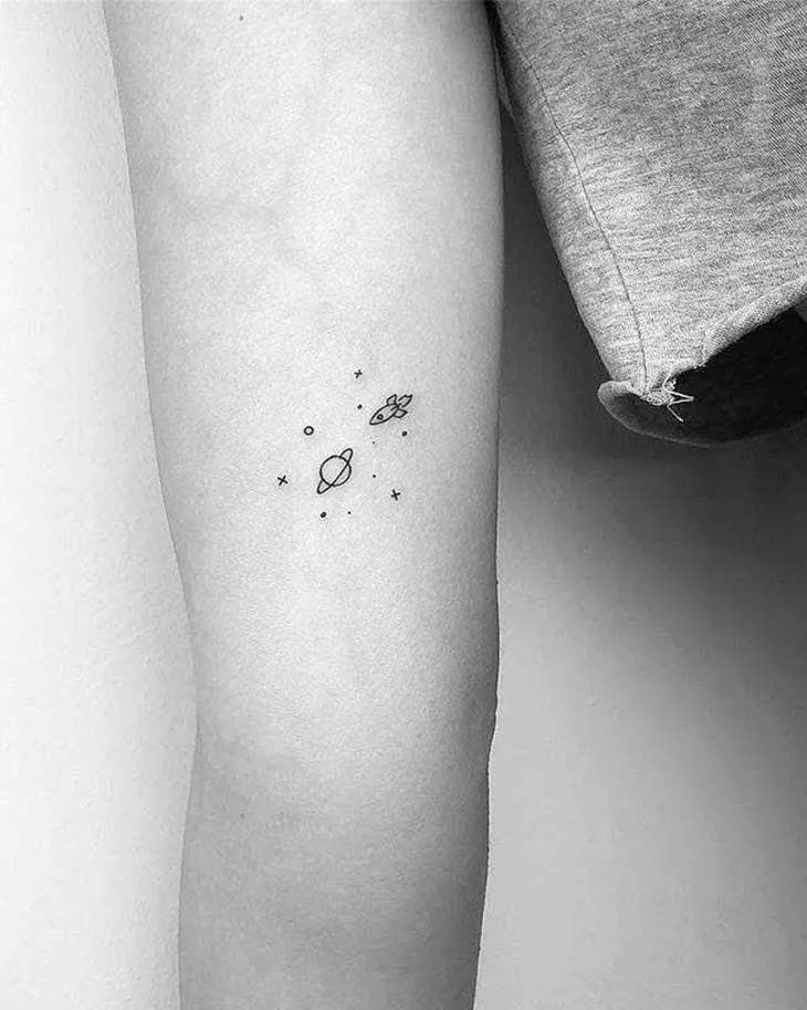 Tatouage minimaliste d’une planète, des étoiles et d’une fusée à l’arrière du bras