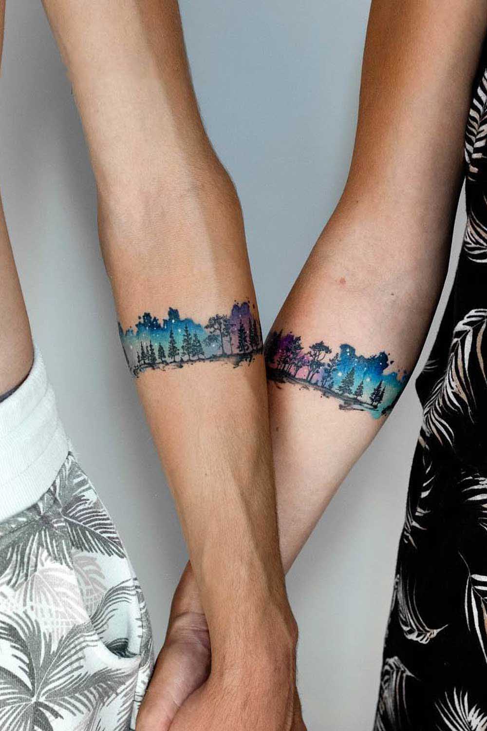 Deux tatouages similaires qui représentent une forêt avec un ciel étoilé multicolore