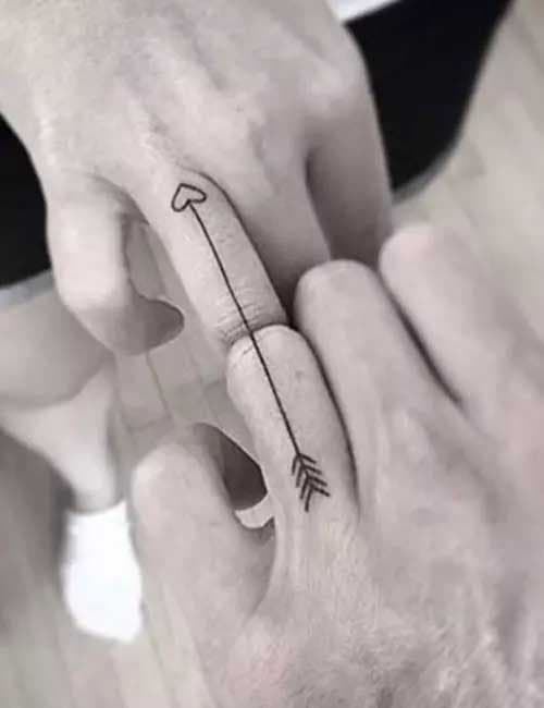 Deux tatouages très simples en forme de flèche qui se complètent d’un doigt à l’autre