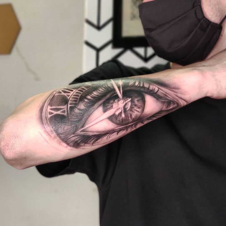 Tatouage des aiguilles d’une montre au centre d’une pupille sur l’avant-bras 